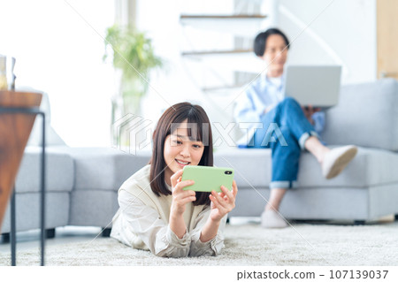 Friendly young couple relaxing in the living room while looking at their smartphones Friendly young couple relaxing in the living room while looking at their smartphones 107139037