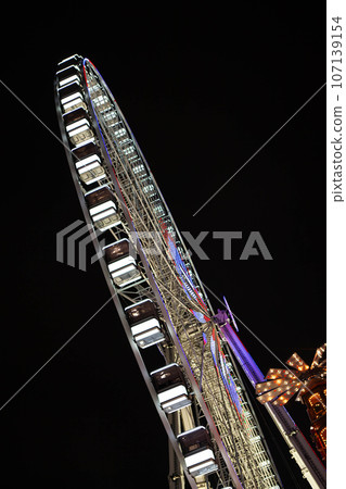 Illuminated ferris wheel at a funfair. Illuminated ferris wheel at a funfair. 107139154