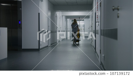 Adult nurse pushes cleaning trolley down medical center hallway Adult nurse pushes cleaning trolley down medical center hallway 107139172