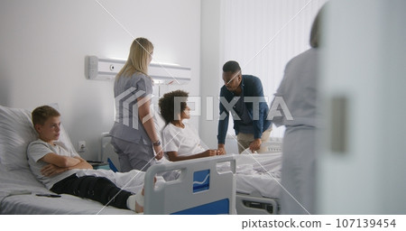 Mature physician bandages leg of young boy Mature physician bandages leg of young boy 107139454