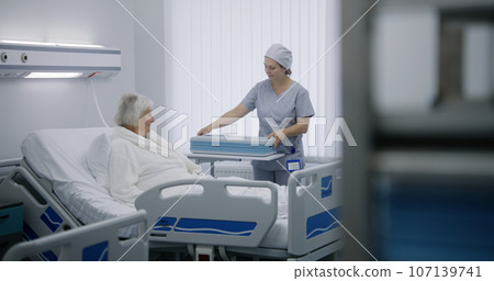 Nurse opens big lunch box with meal to female old patient 107139741