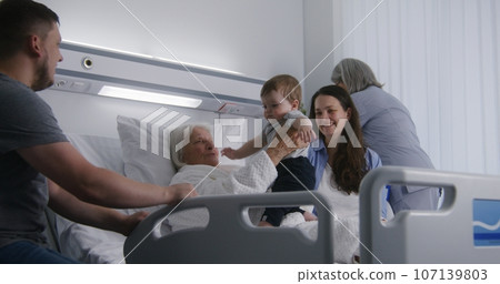 Elderly woman lies in bed in hospital ward, plays with grandson Elderly woman lies in bed in hospital ward, plays with grandson 107139803