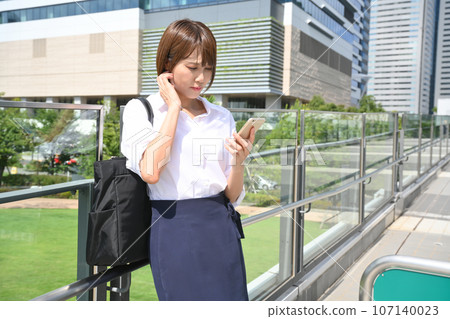 A woman stops on a pedestrian bridge and looks at her smartphone 107140023