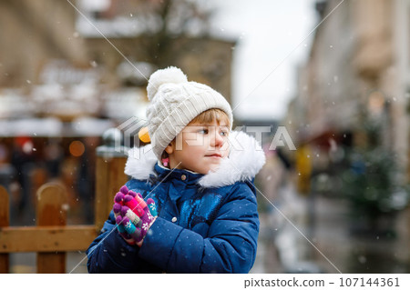 Little cute preschool girl on Christmas market. Happy child on traditional family market in Germany. Preschooler in colorful winter clothes during snowfall 107144361
