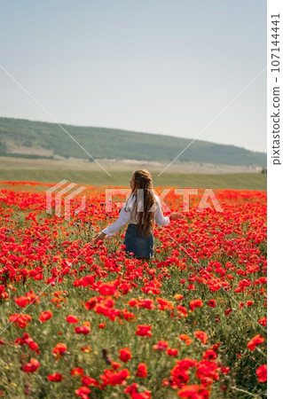 Woman poppies field. Back view of a happy woman with long hair in a poppy field and enjoying the beauty of nature in a warm summer day. 107144441