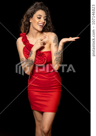 Cheerful young woman in red dress pointing to her open palm Cheerful young woman in red dress pointing to her open palm 107146823