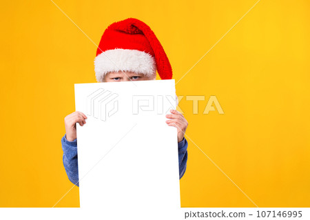 Cute little girl in Santa Claus hat with a white blank paper sheet. Christmas, x-mas, New Year, Winter, people, advertisement, sale concept. Cute little girl in Santa Claus hat with a white blank paper sheet. Christmas, x-mas, New Year, Winter, people, advertisement, sale concept. 107146995