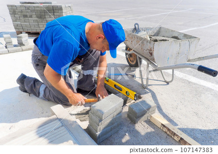 Professional bricklayer works at construction site and lays brick foundation. Man in uniform is Professional bricklayer works at construction site and lays brick foundation. Man in uniform is 107147383