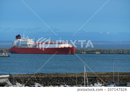 LNG or liquified natural gas carrier moored by industrial pier on hazy evening. Alternative gas supply, commercial freight, energy crisis, regasification, diversification, fuel and energy generation.  107147826
