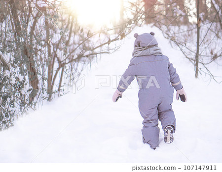 A little girl is walking in the park on the snow winter day. A little girl is walking in the park on the snow winter day. 107147911