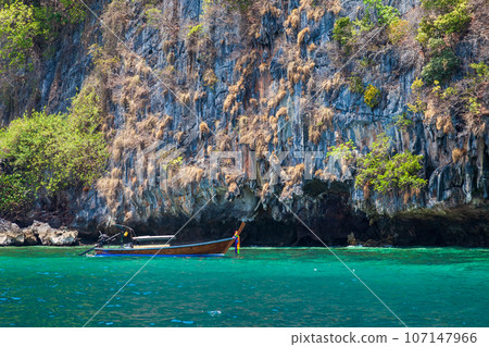 Old traditional Thai motorboat made of wood for fishing and tourists on excursions in the Andaman Sea near Phi Phi Leh island in clear turquoise water under a blue sky. Travel and vacation in phuket. Old traditional Thai motorboat made of wood for fishing and tourists on excursions in the Andaman Sea near Phi Phi Leh island in clear turquoise water under a blue sky. Travel and vacation in phuket. 107147966
