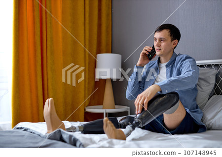 disabled male with artificial leg talking on phone at home. adult guy with prostheses 107148945