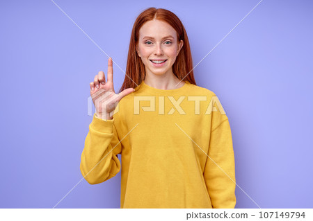 cheerful redhead woman in yellow stylish sweater demonstrating letter L cheerful redhead woman in yellow stylish sweater demonstrating letter L 107149794