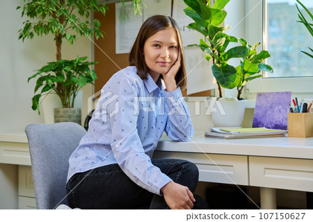 Portrait of young positive woman looking at camera, sitting on chair at home Portrait of young positive woman looking at camera, sitting on chair at home 107150627