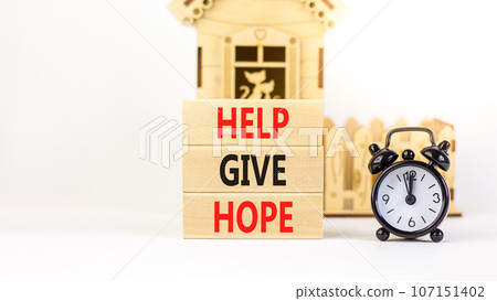 Help give hope symbol. Concept word Help give hope on beautiful wooden block. Black alarm clock. Beautiful white table white background. Business motivational help give hope concept. Copy space. Help give hope symbol. Concept word Help give hope on beautiful wooden block. Black alarm clock. Beautiful white table white background. Business motivational help give hope concept. Copy space. 107151402
