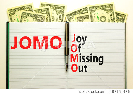 JOMO joy of missing out symbol. Concept words JOMO joy of missing out on book on beautiful white background. Dollar bills. Business JOMO joy of missing out concept. Copy space. 107151476