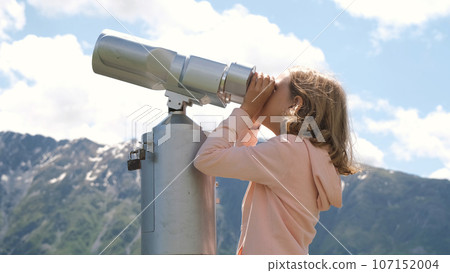 Teen girl looking at scenic view of mountains with binoculars 107152004