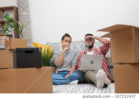tired Couple in their home, laptop amidst boxes, online decor shopping after moving in creating their ideal sanctuary or coordinating their move 107152437
