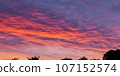 The horizon's silhouette is framed by the vibrant hues of monsoon clouds during sunset 107152574