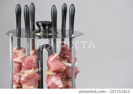 Cooking pork meat in an electric kebab maker on vertical skewers 107152823