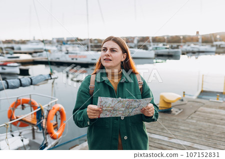 Confused traveler looking at city map, got lost. Upset lady lost, checking map in Gdansk. Traveling Europe in spring. Woman with map walking along the waterfront, seaside. High quality photo 107152831
