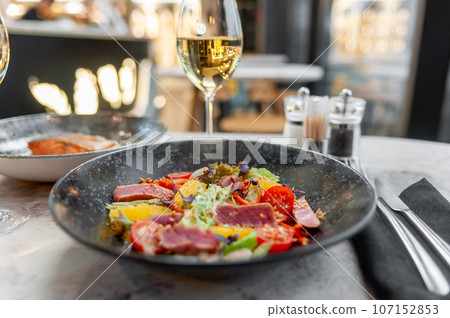 Tuna tataki salad with lettuce, tomatoes and orange on a marble table 107152853