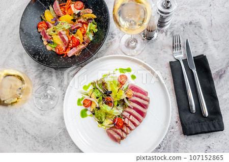 two plates with tuna tataki salad with lettuce, avocado and cherry tomatoes 107152865
