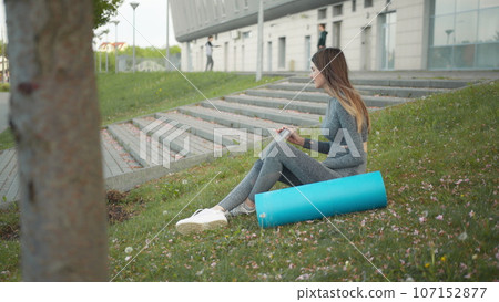 Happy woman, sitting laptop outdoor. Smiling fit girl typing on laptop computer at city background. Person working on laptop outside. Attractive girl, corporate startup office employee working outdoor Happy woman, sitting laptop outdoor. Smiling fit girl typing on laptop computer at city background. Person working on laptop outside. Attractive girl, corporate startup office employee working outdoor 107152877