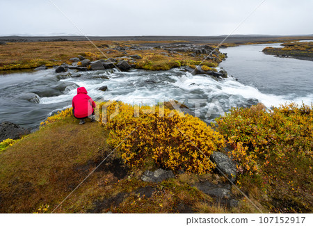 Woman in red raincoat at Grafarlandsfoss falls in northern Iceland highlands. Woman in red raincoat at Grafarlandsfoss falls in northern Iceland highlands. 107152917
