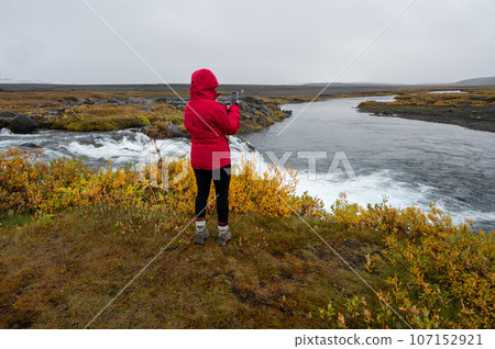 Woman in red raincoat at Grafarlandsfoss falls in northern Iceland highlands. 107152921