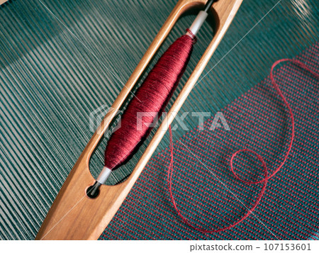 Interweaving of green warp threads and red weft threads, close up. Weaving loom, yarn and boat shuttle 107153601