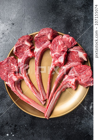 Lamb chop rib steak, raw mutton meat cutlet in golden plate. Black background. Top view Lamb chop rib steak, raw mutton meat cutlet in golden plate. Black background. Top view 107155074