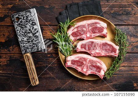 Uncooked Raw lamb loin chops steaks, saddle in plate with rosemary and thyme. Wooden background. Top view Uncooked Raw lamb loin chops steaks, saddle in plate with rosemary and thyme. Wooden background. Top view 107155090