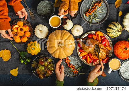 Thanksgiving festive table composition, friends or family eating together roasted turkey, vegetable salad, fruit, orange beverage. Celebration dinner with traditional autumn meals on rustic dark table 107155474