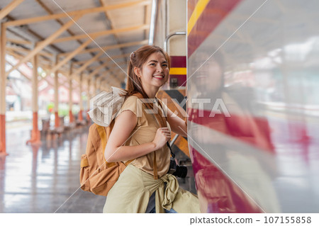 Beautiful asian traveler with backpack getting on a train at a platform of railway station 107155858