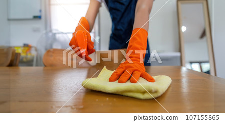 Asian woman wear rubber protective orange gloves sit clean guest reception desk with product and equipment cleaner at home Asian woman wear rubber protective orange gloves sit clean guest reception desk with product and equipment cleaner at home 107155865