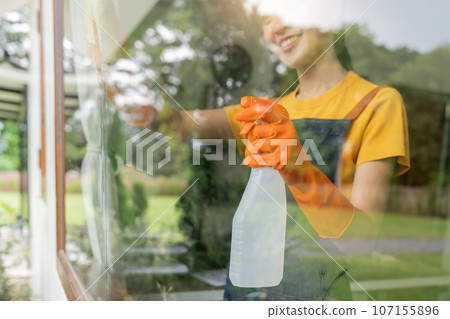 Young Asian housewife cleaning window glass with rags and detergent spray, cleaning house on the weekend Young Asian housewife cleaning window glass with rags and detergent spray, cleaning house on the weekend 107155896