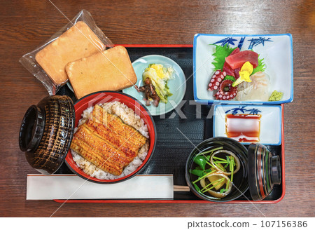 [Materials] Overhead shot of a Japanese meal set that includes eel bowl, sashimi, soup, and baked cookies. 107156386