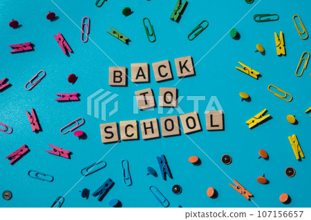 BACK TO SCHOOL message inscription text on wooden blocks on creative colorful blue background with stationery supplies around. Educational greeting announcement for students and teacher. Top view flat BACK TO SCHOOL message inscription text on wooden blocks on creative colorful blue background with stationery supplies around. Educational greeting announcement for students and teacher. Top view flat 107156657