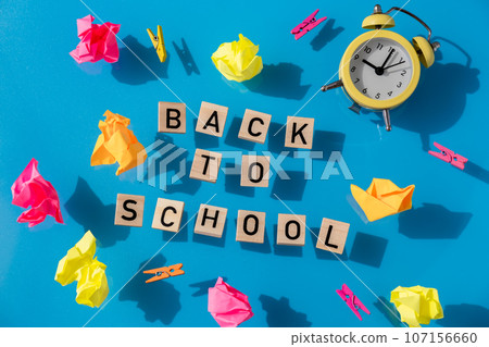Educational greeting announcement for students and teacher. Saying BACK TO SCHOOL text on wooden blocks on colorful blue background around stationery supplies and alarm clock.Top view flat lay Concept 107156660