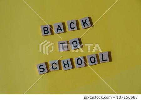 Educational greeting announcement for students and teacher. Saying BACK TO SCHOOL text on wooden blocks on colorful yellow background. Top view flat lay Concept of new school year 107156665