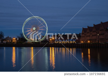 Gdansk Poland Ferris wheel in the old town of Gdansk at night evening dusk Reflection in river water Europe. Long exposure photo. City scenic view Illuminated attraction park and street 107156691