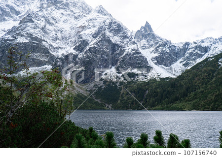 Morskie Oko lake Snowy Mountain Hut in Polish Tatry mountains, Zakopane, Poland. Beautiful green hills and mountains in dark clouds and reflection on the lake Morskie Oko lake 107156740
