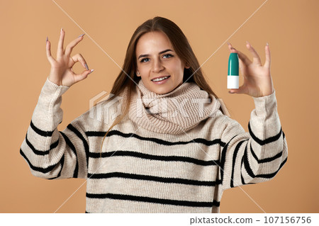 woman holds nasal spray for allergies on beige background 107156756