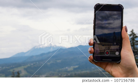 Mobile phone shooting video for social media. Tourist blogger travel hand making memories Snowy mountains, green forests In National park. Mountain nature landscape. Travel outdoors green tourism Mobile phone shooting video for social media. Tourist blogger travel hand making memories Snowy mountains, green forests In National park. Mountain nature landscape. Travel outdoors green tourism 107156786