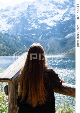 Young woman enjoying nature in Morskie Oko Snowy Mountain Hut in Polish Tatry mountains Zakopane Poland. Naturecore aesthetic beautiful green hills. Mental and physical wellbeing Travel outdoors 107156811