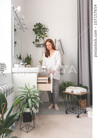 Happy young woman standing near dressing table and taking out a beauty cosmetic from drawer. 107157654