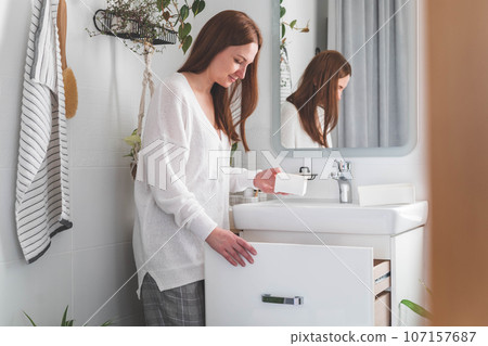 Happy young woman standing near dressing table and taking out a beauty cosmetic from drawer. Happy young woman standing near dressing table and taking out a beauty cosmetic from drawer. 107157687