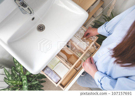 Top view of woman hands neatly organizing bathroom amenities and toiletries in drawer in bathroom. 107157691