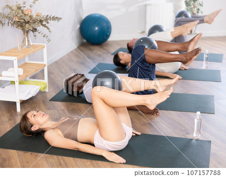 Young woman with multinational group exercising with bender balls at gym 107157788